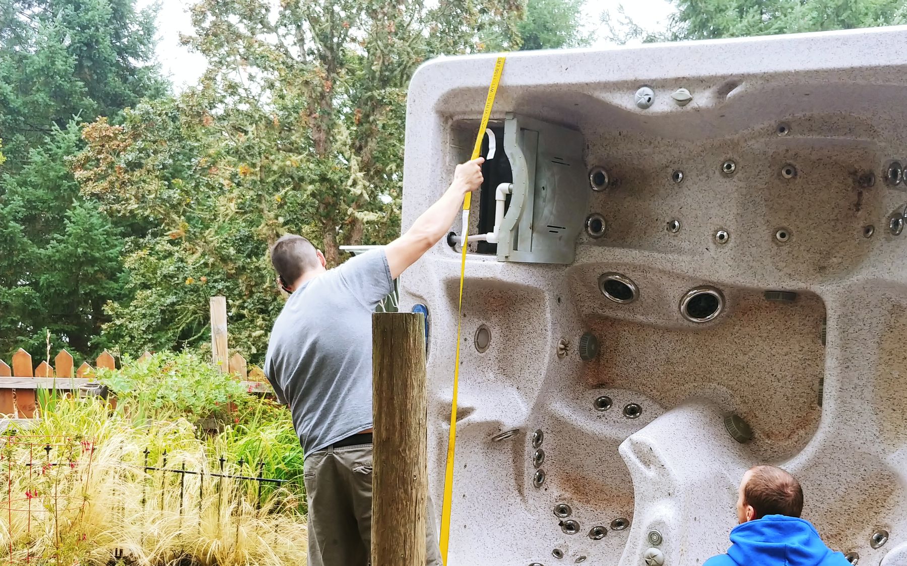 A Confidence mover strapping a hot tub standing on its side in a narrow side yard while another crew member steadies it